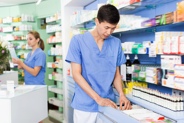Man pharmacist is searching medicine in drawers in apothecary.