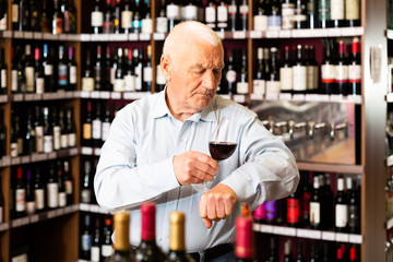 Elderly man checks the color and taste of red wine in a liquor store