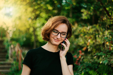 Young hipster girl in glasses talking on the phone outdoors