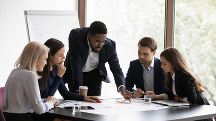 Confident african American male boss work cooperate with diverse team at office briefing, focused biracial businessman head meeting, collaborate discuss business ideas with colleagues at meeting