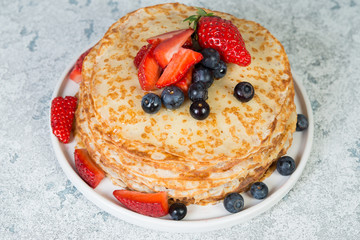 Thin homemade pancakes in a plate with fresh berries and honey.