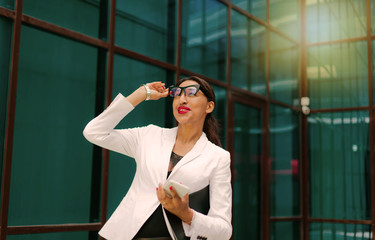 Professional business afro woman in elegant white jacket and skirt with folder with documents in her hands against the background of business center with blue windows