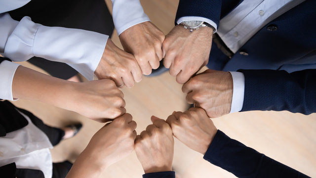 Close up top view of diverse businesspeople join fists involved in business training together, motivated multiracial employees engaged in teambuilding activity, show unity support, teamwork concept