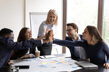 Excited motivated diverse businesspeople give high five show unity and support at company meeting,...