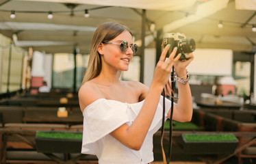 Young smiling woman takes pictures with a retro camera on the background of outdoor cafe