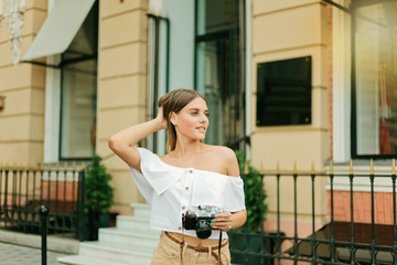 Cheerful blond woman holding retro camera in the urban environment