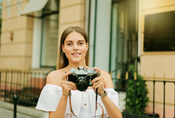 Cheerful blond woman holding retro camera in the urban environment