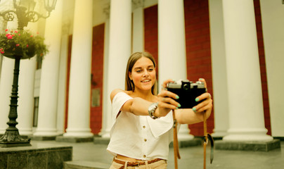 Happy tourist woman takes pictures on the background of the building with columns on retro camera outdoors