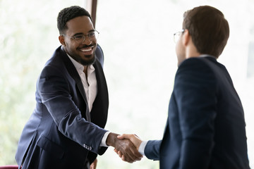 Smiling diverse male business partners shake hands get acquainted greeting at office meeting, happy...