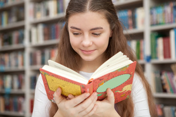 Close up of a charming teen girl smiling, reading a book at local library. Imagination, hobby, relax concept