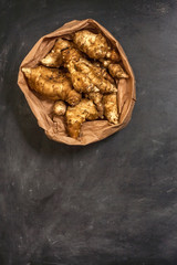 Several Jerusalem artichoke tubers in a paper bag on a black background with copy space. Helianthus tuberosus. Top view