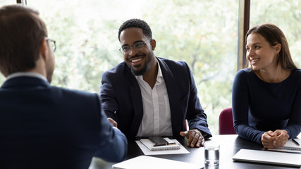 Smiling African American male employee shake hand of colleague greeting getting acquainted at office meeting, happy diverse businessman handshake close deal after successful negotiations at briefing