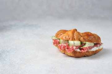 Croissant with salami, ricotta and fresh cucumber. Light background. Close-up. Free space for text.