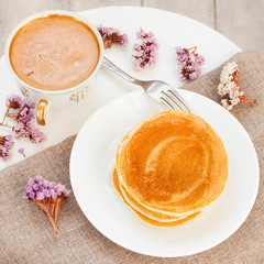Cup coffee, honey pancakes on plate, flowers and tablecloth on a white coffee table. Gentle good morning. Tasty breakfast