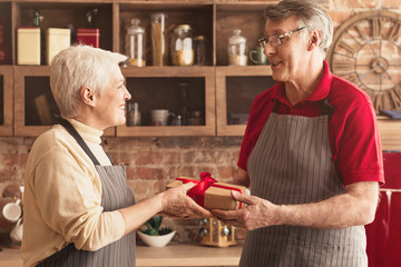 Loving Senior Man Greeting Wife With Anniversary, Giving Gift In Kitchen