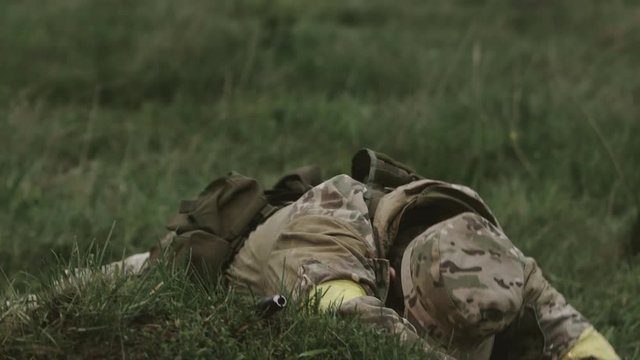 Soldier Looks At The Sight Of The Weapon. Man In Camouflage Clothing Lies In The Grass.