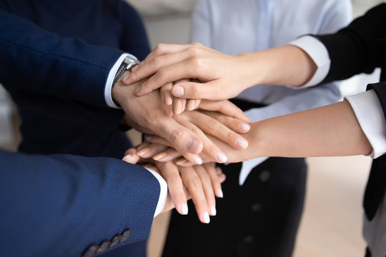 Close up of diverse businesspeople stack hands show unity and support in work, supportive motivated multiracial colleagues coworkers engaged in teambuilding activity at meeting, teamwork concept