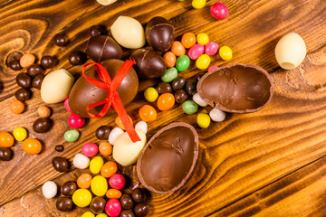 Chocolate easter eggs and multicolored candies on wooden table. Top view