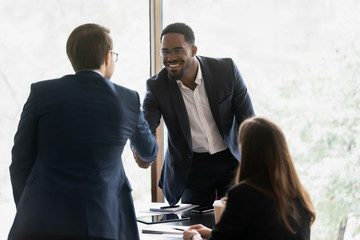 Smiling multiracial male business partners handshake greeting getting acquainted at office meeting,...