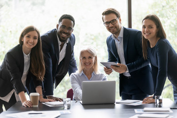 Group portrait of smiling multiracial team gather at desk in boardroom working together on business project in office, happy multiracial businesspeople posing cooperating in shared workplace - obrazy, fototapety, plakaty