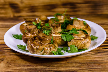 Plate with baked champignons, dill and parsley on a wooden table