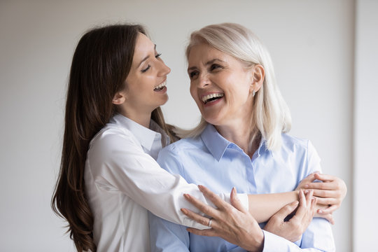 Overjoyed senior mother and grown-up daughter hug embrace enjoying leisure time together, smiling mature mom and adult girl child cuddle have fun laugh at home, good parenthood concept