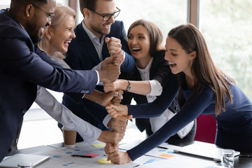 Overjoyed diverse businesspeople stack fist engaged in funny teambuilding activity at office meeting together, happy motivated multiracial employees join hands show unity and support, teamwork concept