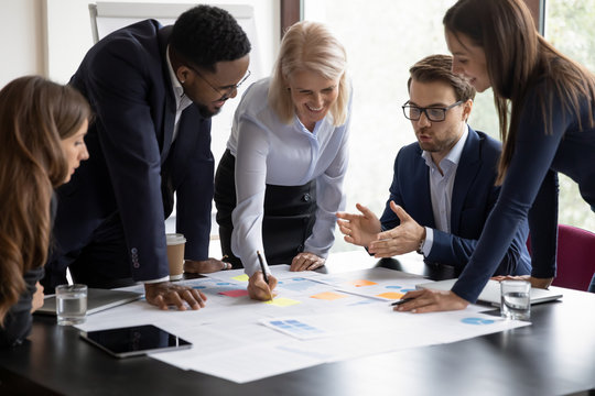 Happy motivated diverse businesspeople work together cooperate at business office meeting, smiling multiracial colleagues discuss ideas financial project at boardroom briefing, collaboration concept