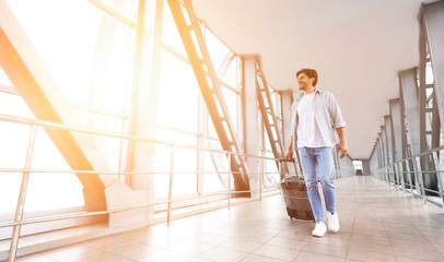 Fototapeta premium Happy man walking with suitcase in airport terminal