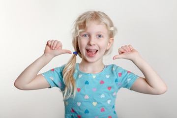 Portrait of beautiful little funny joyful blonde Caucasian girl on a light background. Happy smiling preschool child kid showing like thumb fingers. Positive emotion face expression.