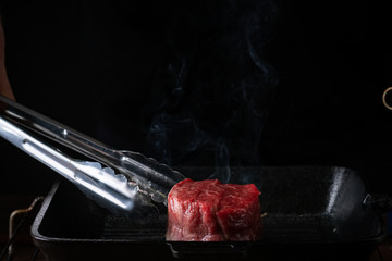 Filet Mignon steak in a pan is turned over with tongs, the process of cooking on the grill