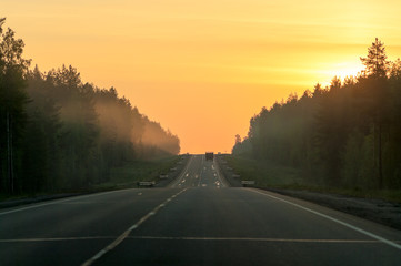 Beautiful orange sunrise above countryside highway and lorry on road at the distance