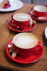 World Coffee Day concept. Hot coffee mocha with beautiful latte art topping in red ceramic cups on wood table in coffee shop. Selective focus. 