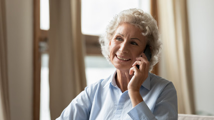 Happy senior 60s woman feel excited optimistic talking on smartphone gadget at home, smiling mature...