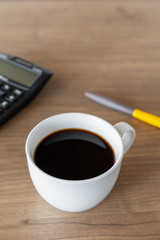 hot coffee cup, pen and black calculator on wooden table background. top view