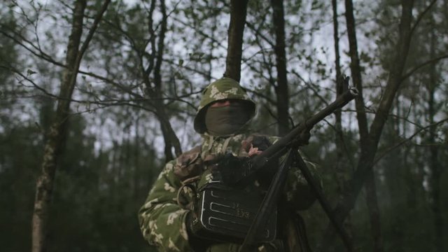 Soldier Stands In The Woods And Shoots From Machine Gun.
