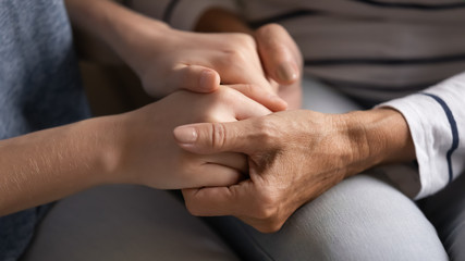 Close up of senior mom and adult daughter hold hands talk tell secrets enjoy family time together, mature mother and grownup young woman child show love, care and support, share close intimate moment