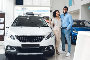 Husband And Wife Holding New Automobile Key Standing In Dealership
