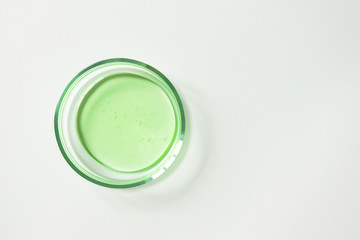 Transparent green shampoo or facial cleaner in glass petri dish on white background, top view. Concept laboratory tests and research, making natural cosmetic