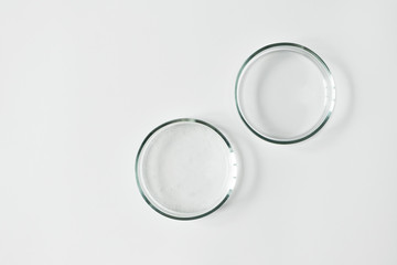 Two glass petri dish with transparent gel with air bubbles and one empty on white background, top view and copy space. Concept laboratory tests and research, making cosmetic