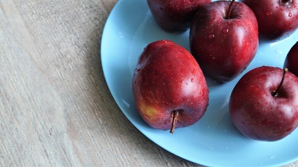 red ripe apples in drops of water on a blue dish on a wooden table 