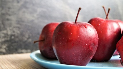 red ripe apples in drops of water on a blue dish on a wooden table on a black background