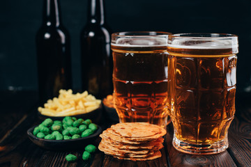 Appetizing beer snacks close up. Crunchy salty nuts, crackers and corn with two mugs of lager. Oktoberfest food, pub concept