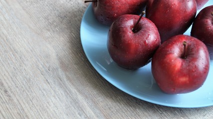 red ripe apples in drops of water on a blue dish on a wooden table 