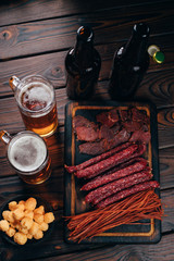 Appetizing beer snacks selection. Sausages, cheese crunches, dried meat on wooden board. Oktoberfest food, pub concept