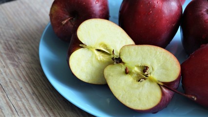 red ripe apples in drops of water on a blue dish on a wooden table 