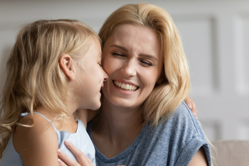 Overjoyed young mother and cute little preschooler daughter feel playful hugging cuddling at home, happy mom and small girl child play have fun enjoy family weekend together in living room