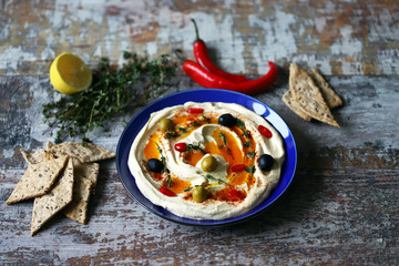 Hummus with olives, paprika and olive oil on a plate. Blue plate serving hummus.