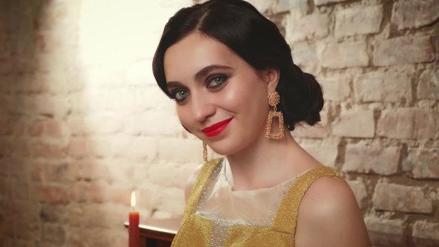 portrait young woman with retro cold finger wave hairstyle. Girl in gold dress, bright evening makeup red lips blue eyes brown shades sparkling vintage earrings. Creative carnival party 1920s style