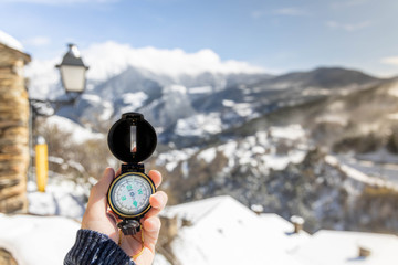 Naklejka premium Hand holding a vintage compass in a snowy mountain village Travel concept. Selective focus and copy space